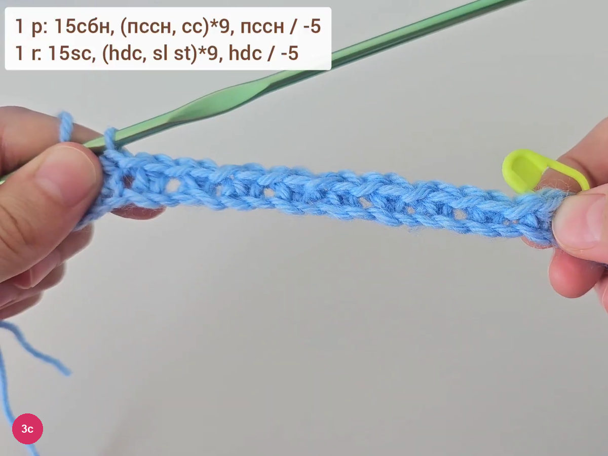Finished first row held between fingers with a stitch marker at its end and unworked chains at the far end