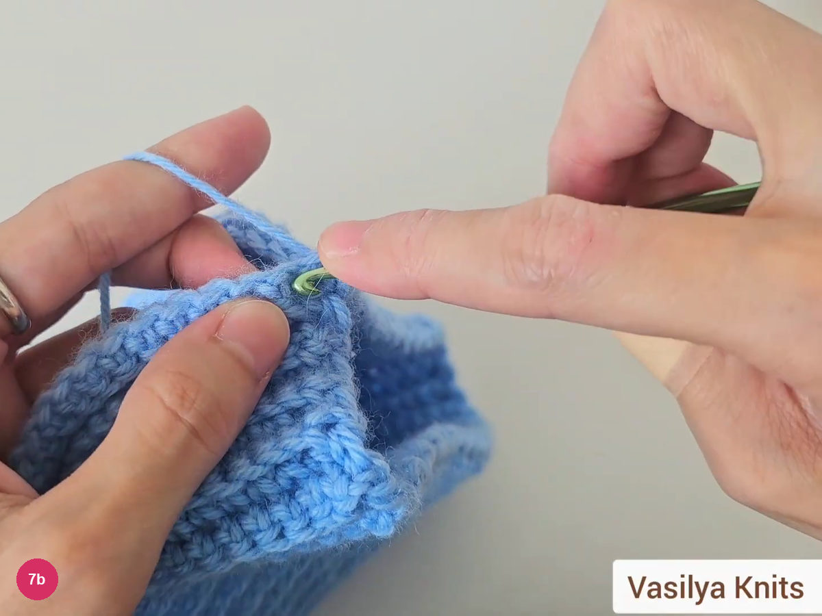 Hook pulling loops through the edge of the folded blue hat to form the seam