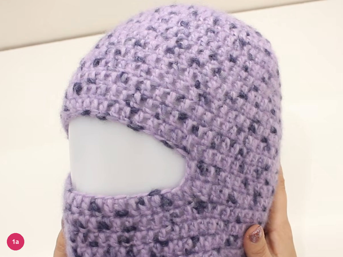 Lilac crochet balaclava on a blank white head form, with an open eye slot and a neck section below it