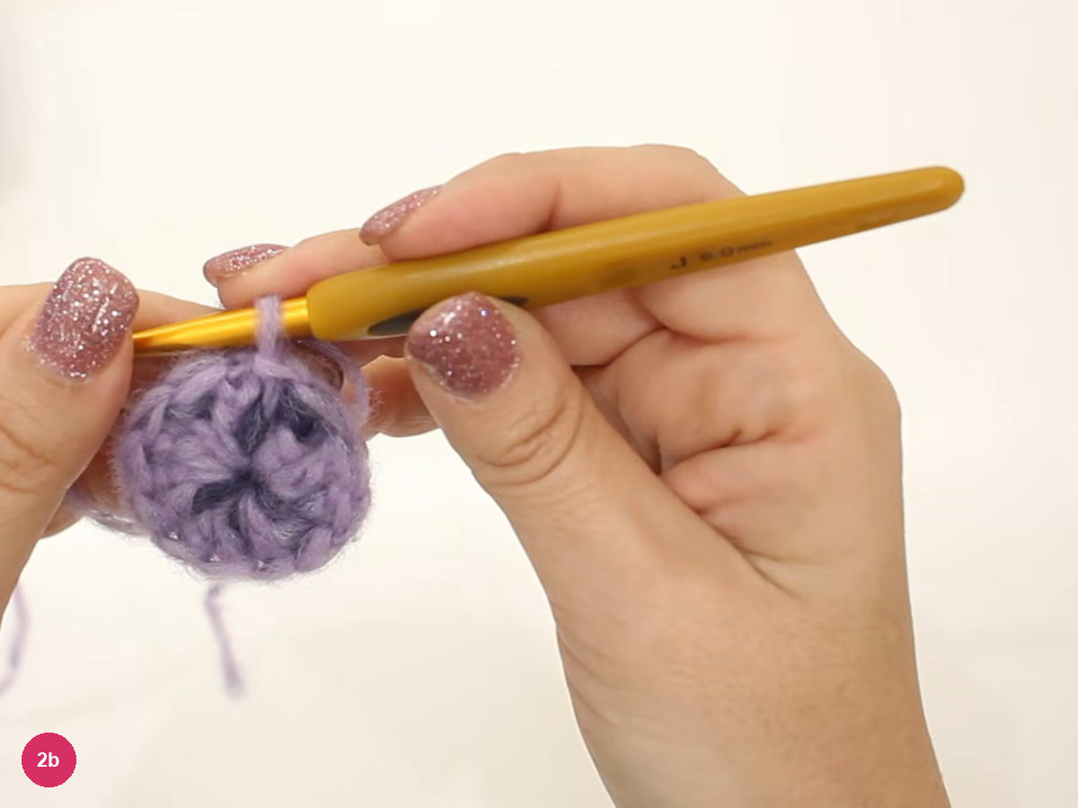 Small closed lilac crochet disc with a dark star-shaped centre held beneath a 6.0 mm gold hook