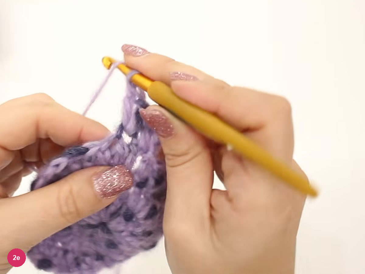 Hook raised above the edge of the larger lilac disc as a stitch of round four is started