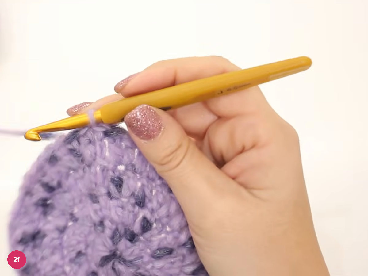 Large lilac crochet disc with the hook resting at its upper edge at the start of round five