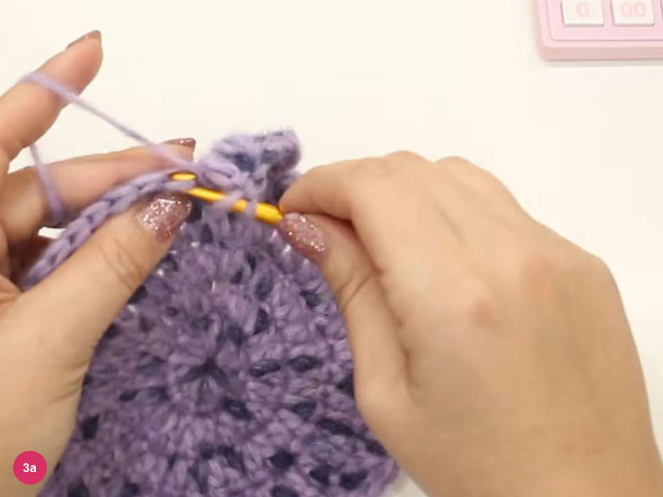 Hook entering the edge of the flat lilac crown as double crochet is worked without increases