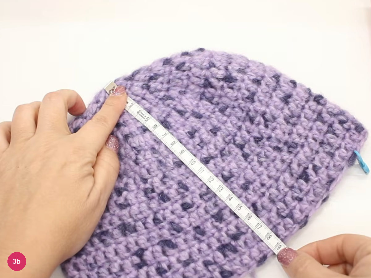 Tape measure lying diagonally across the lilac crochet cap with the 19 cm mark at its lower end