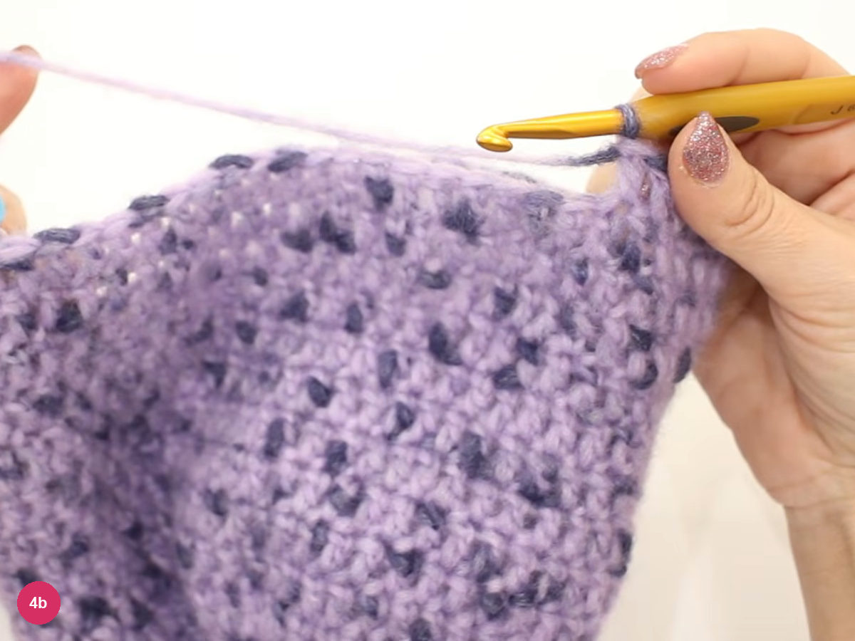 Hook at the top edge of the lilac cap with a long strand of yarn stretched across the rim