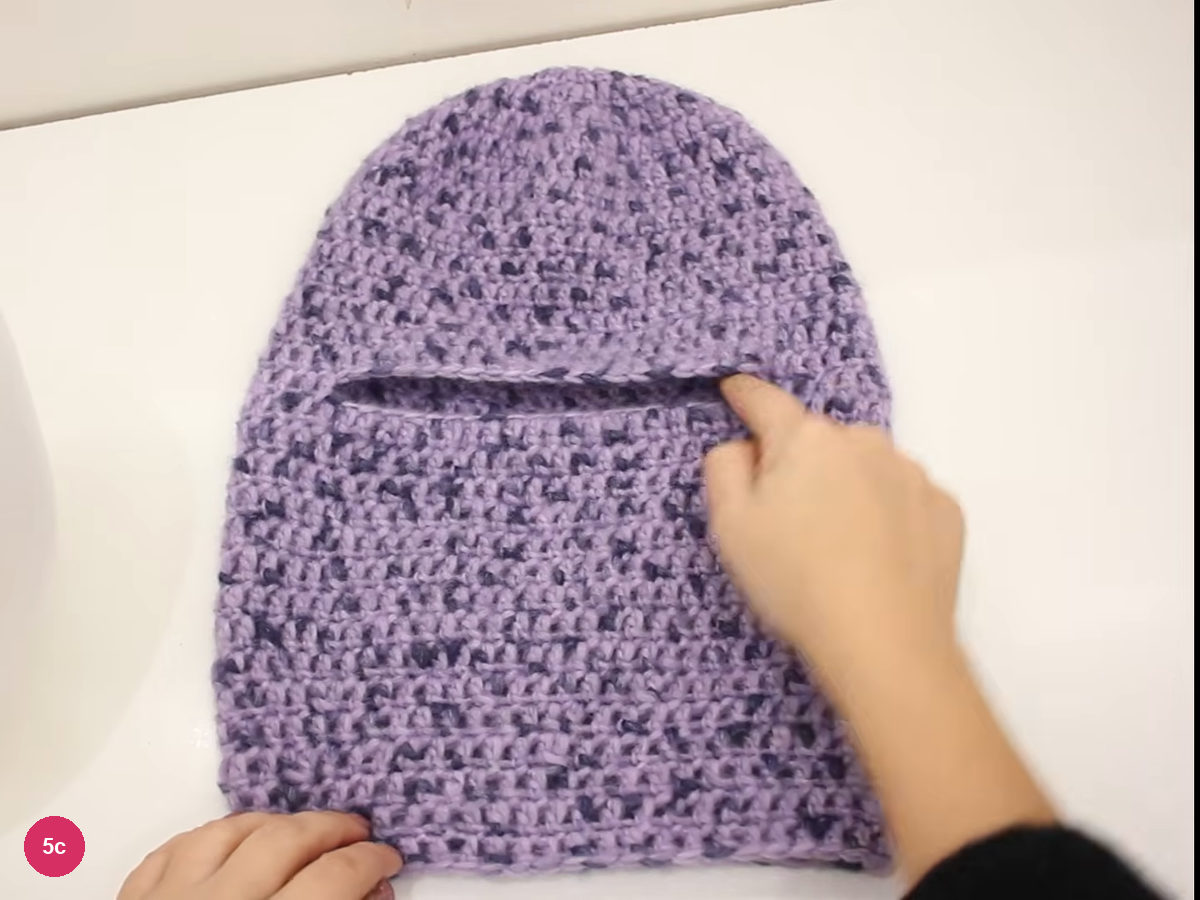 Finished lilac balaclava laid flat on a white table with a horizontal opening between the cap and the neck section