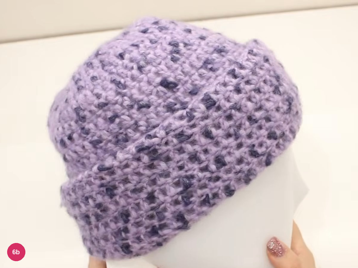 Lilac crochet hat with a thick rolled cuff on a white head form, seen from the side