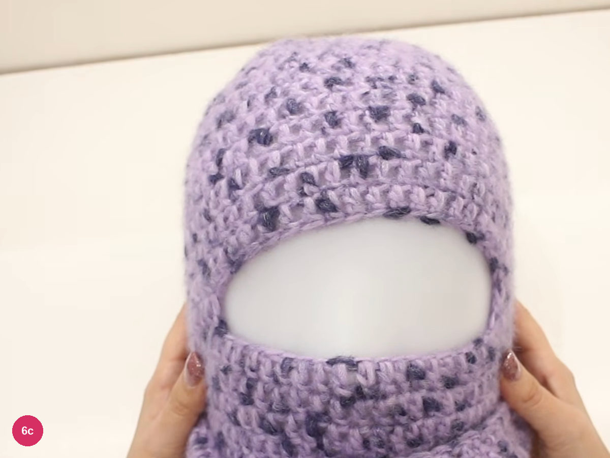 Lilac balaclava on a white head form seen from above the front, with a round opening and the neck section below