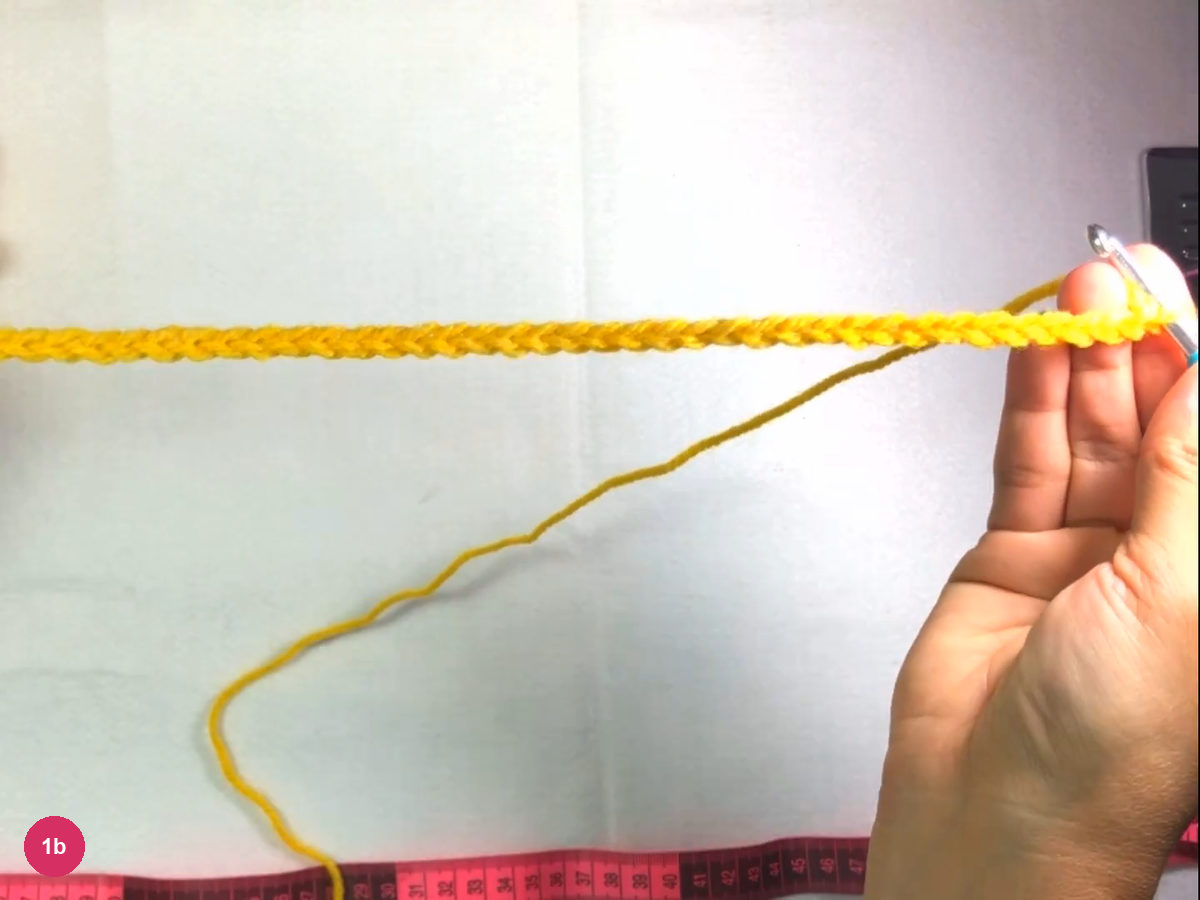 Long yellow chain stretched straight across a white table with the hook resting at its right end