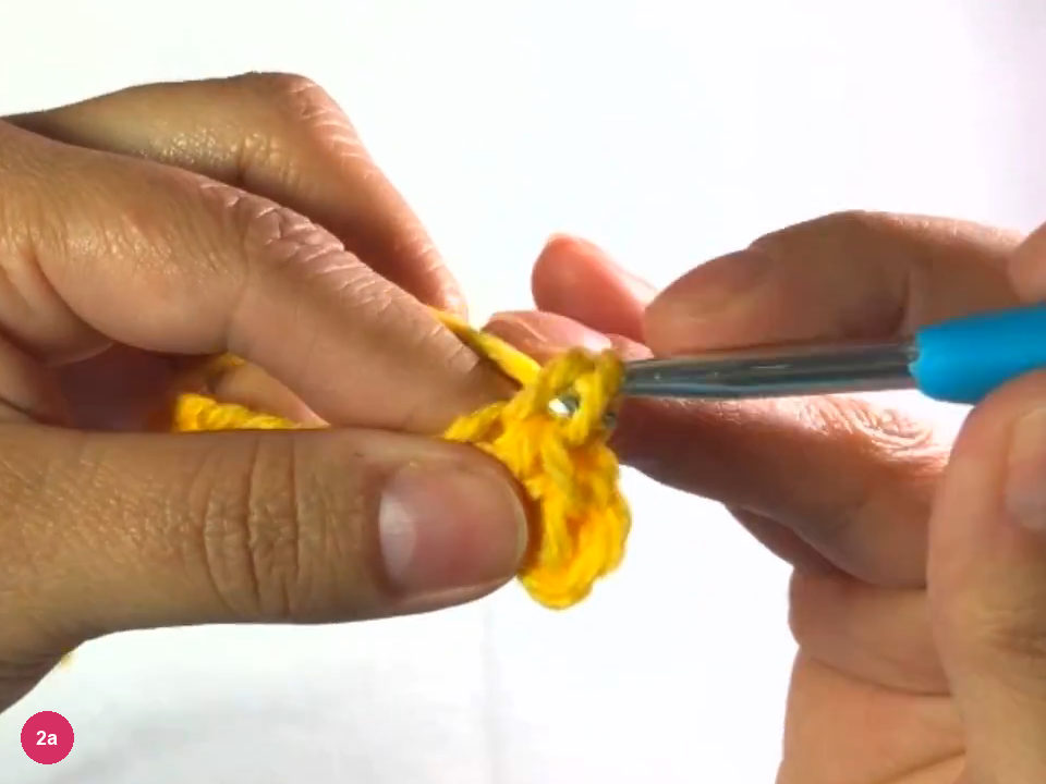 Hook working the first single crochet stitches into the yellow chain between the fingers
