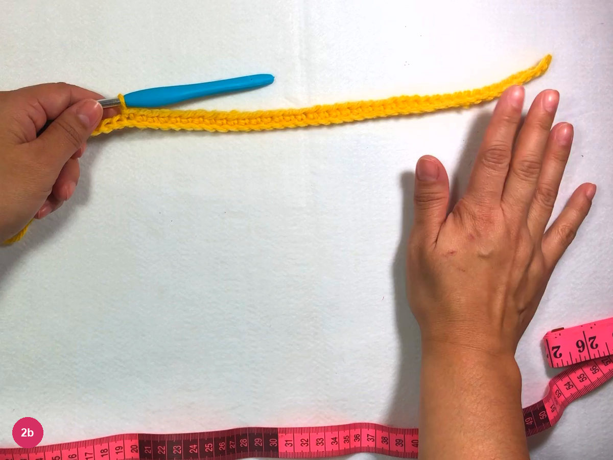 Row of yellow single crochet lying flat beside the hook, with a short unworked chain tail at one end