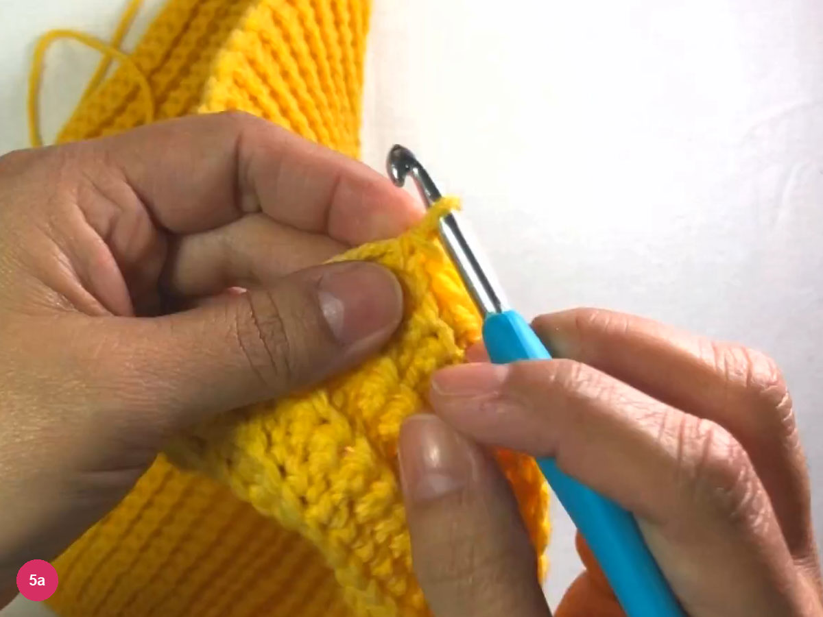 Ribbed yellow piece folded round with the hook held upright beside the two edges that will be joined