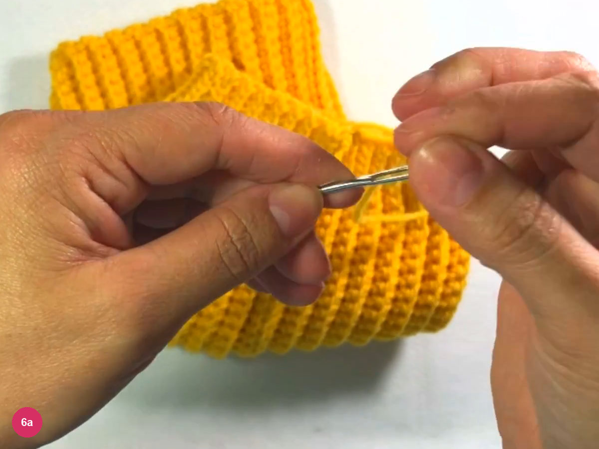 Tapestry needle and yellow yarn tail held beside the open top edge of the ribbed tube