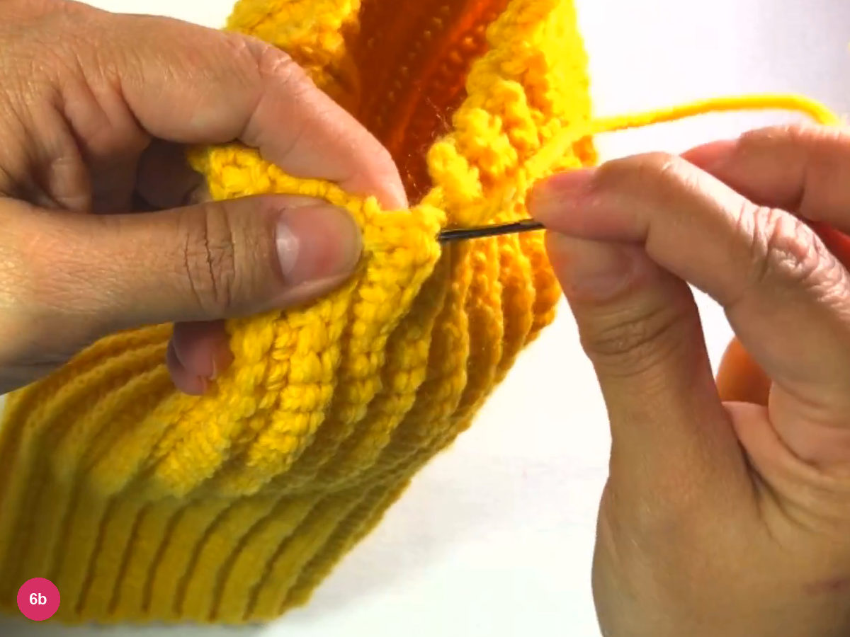 Needle passing through the top edge stitches of the yellow tube with the yarn trailing to the right