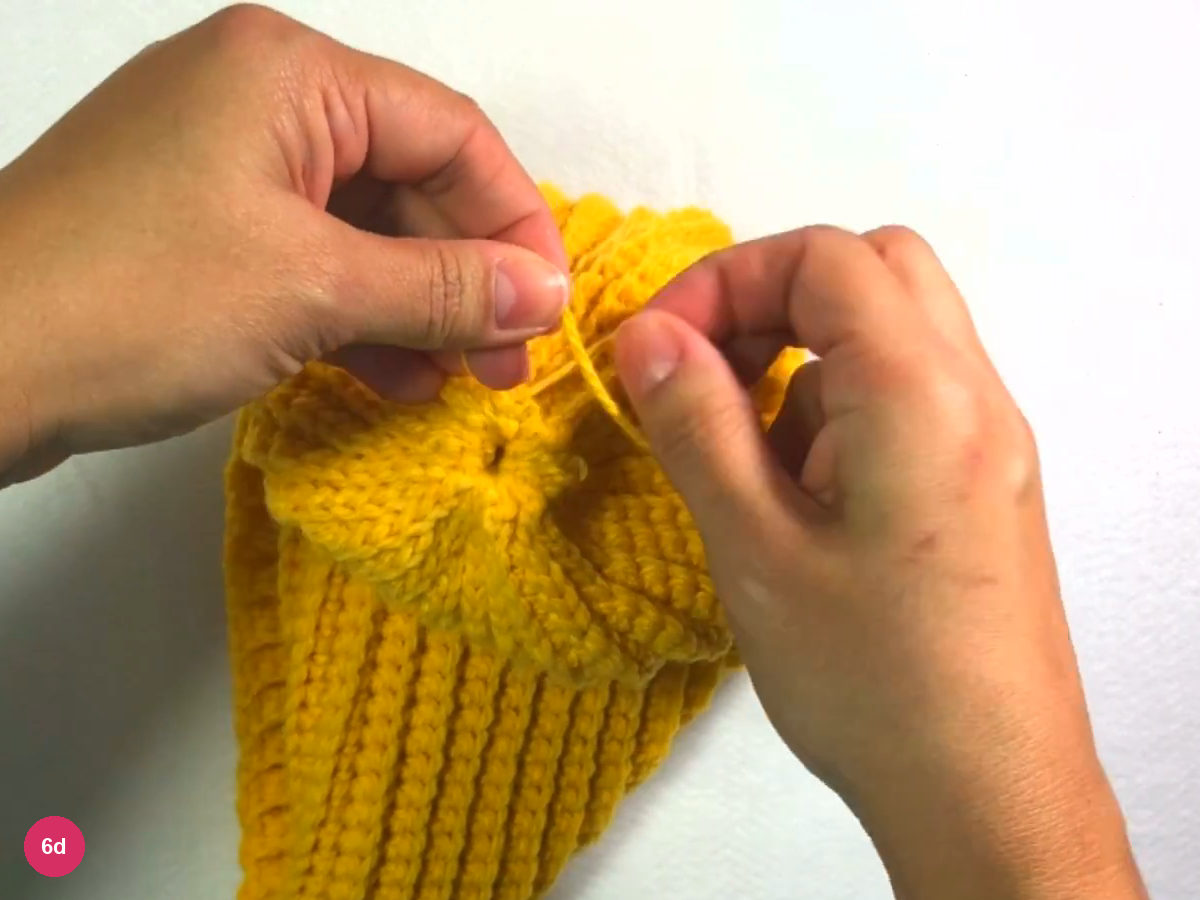 Gathered crown centre with a small opening and the yarn running to the right hand, ribbed tube below