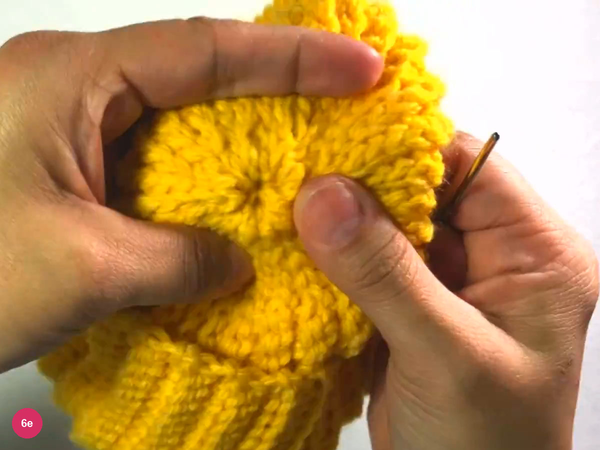 Closed crown of the beanie with ribs radiating from a small centre, held between both hands with the needle at the right