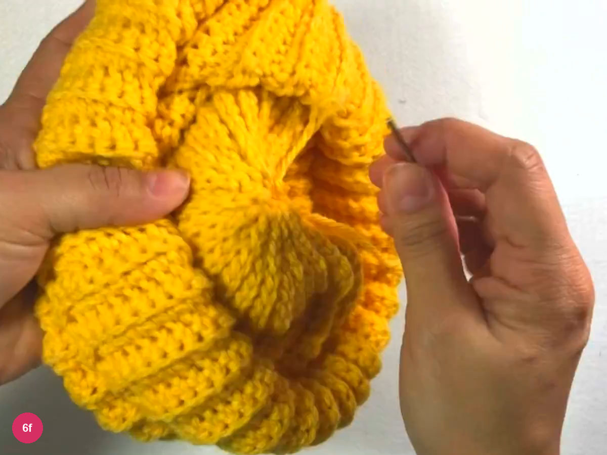 Folded ribbed crown area held in the left hand with the needle at the right, ready to pass through the stitches