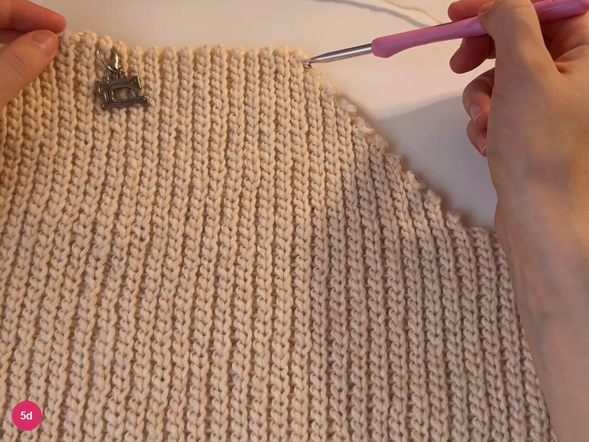 Pink hook held above the top of a broad cream ribbed section
