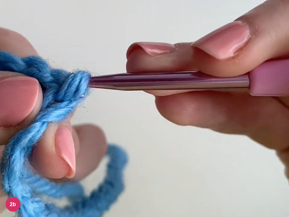 Purple hook drawing blue yarn through the joined chain ends