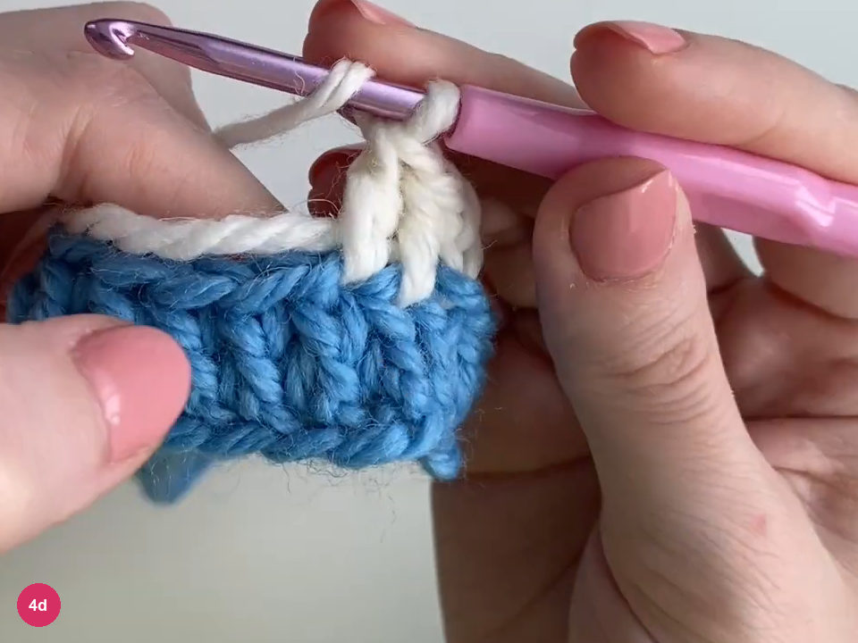 White double crochet posts above the blue round with the hook held over the next stitch