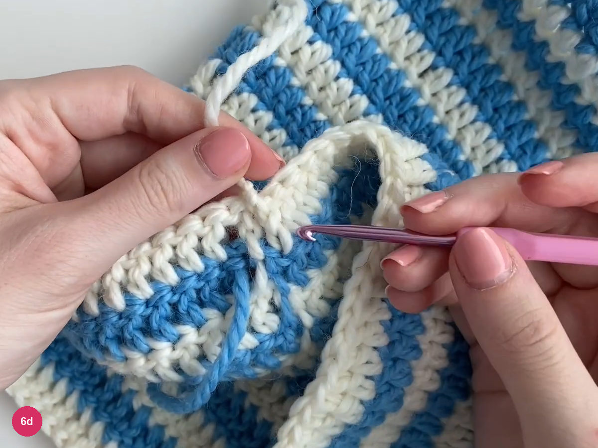 White yarn tails held at the inside edge of the blue-and-white fabric