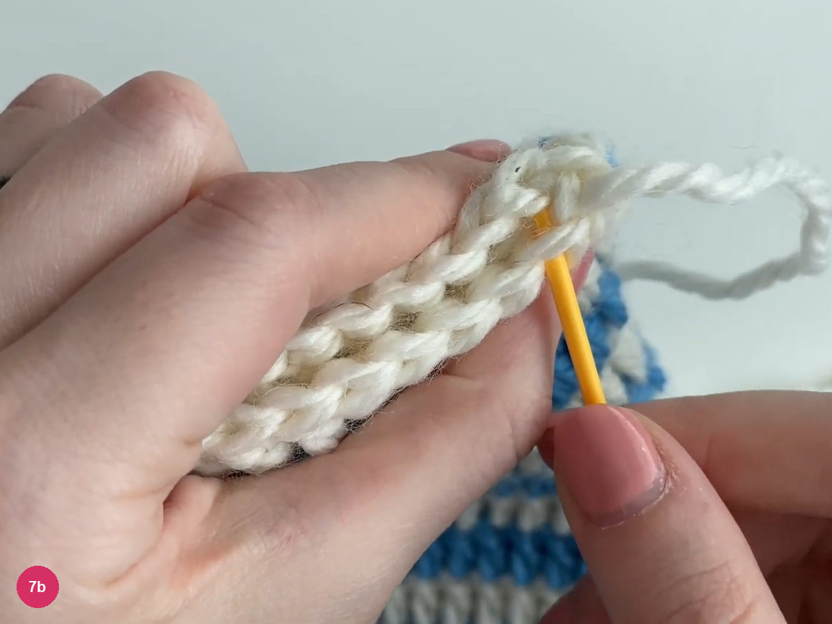 Yellow yarn needle entering the paired white top edges at a corner