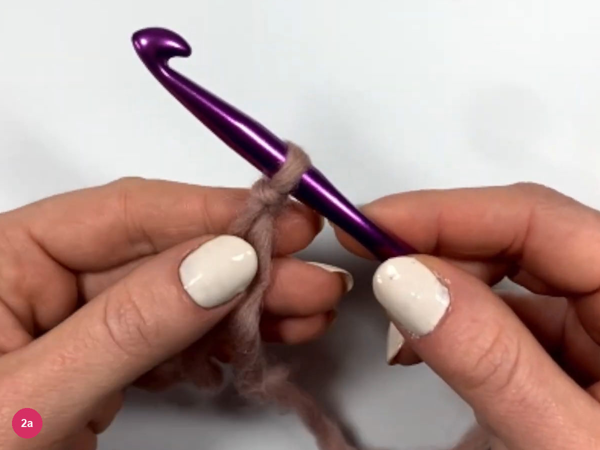 Slip knot sitting on the shaft of a purple crochet hook held between two hands