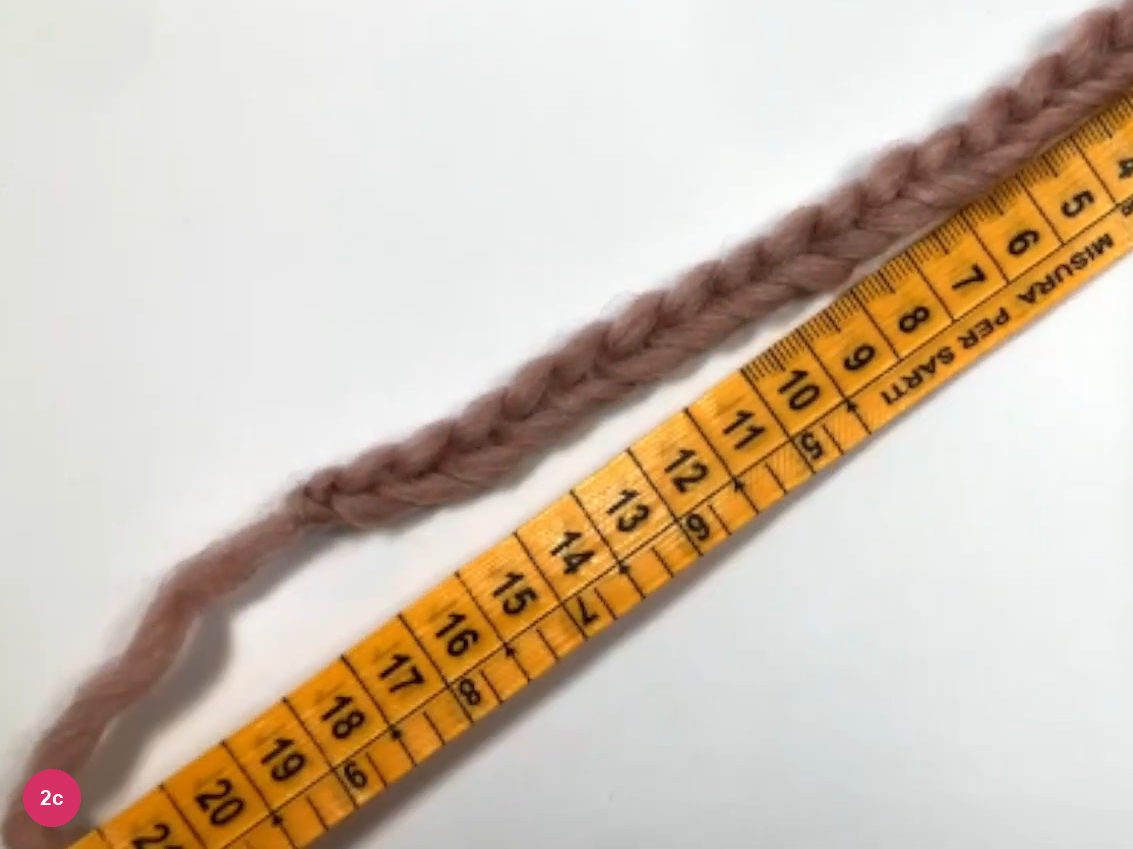Dusty-rose chain lying along an orange tape measure running diagonally, numbers 4 to 20 visible