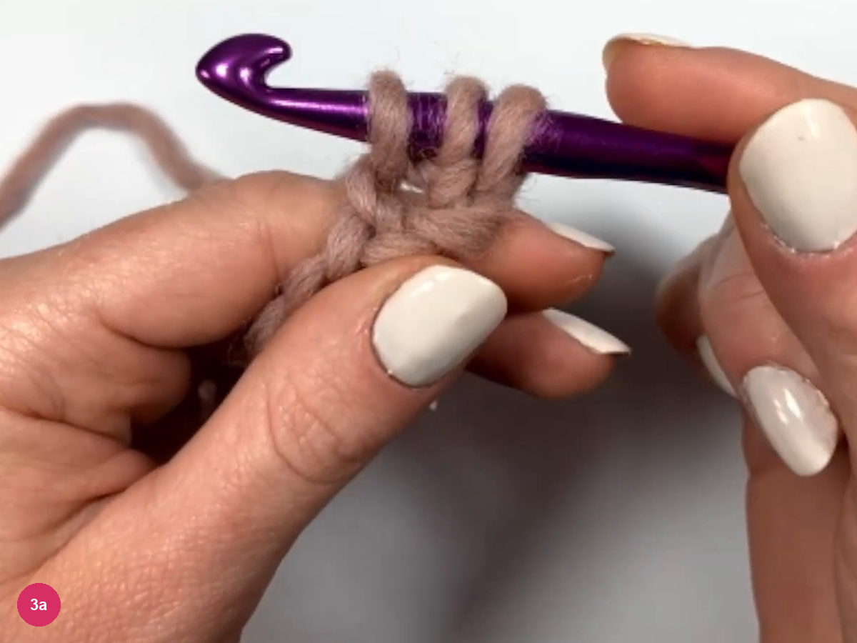 Three loops of rose yarn wrapped on the hook above a short strip of chain held between the fingers