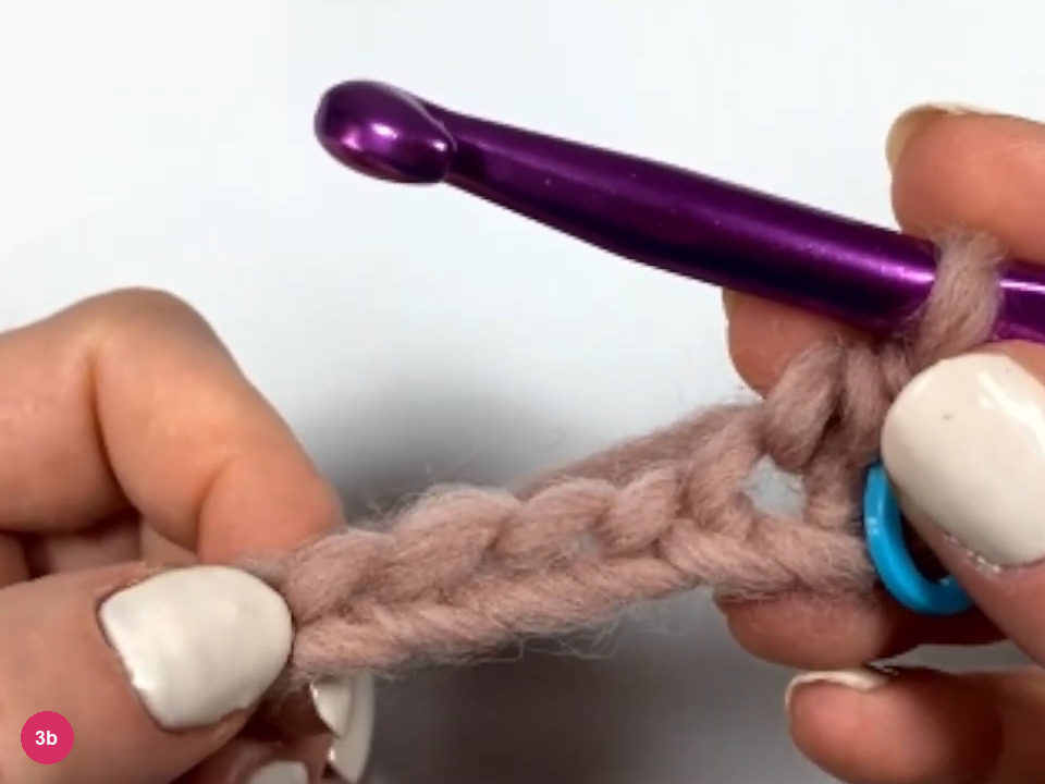 Hook above the first finished stitch of row 1 with a blue stitch marker through the stitch at the end of the chain