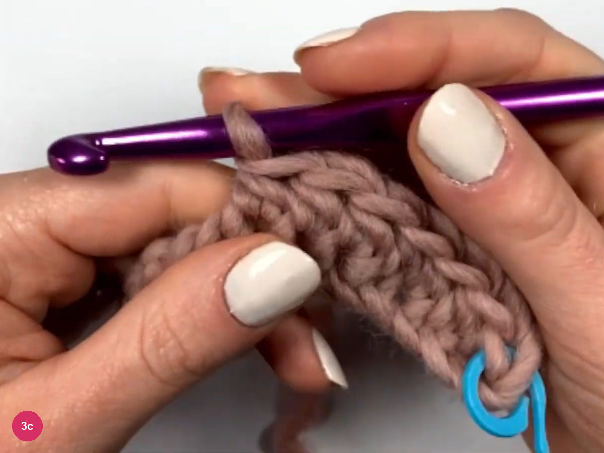 Hook working a half double crochet at the edge of a rose strip, with a blue marker at the lower right end