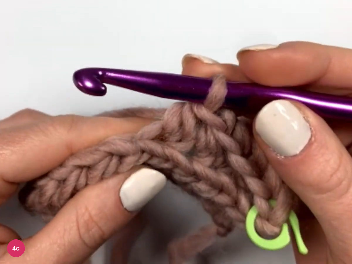 Hook at the top of row 2 above several half double crochet stitches, with a green stitch marker at the end of the row
