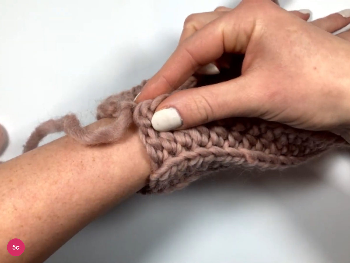 The ribbed panel wrapped around a wrist and held with the other hand, with a yarn tail hanging at the join
