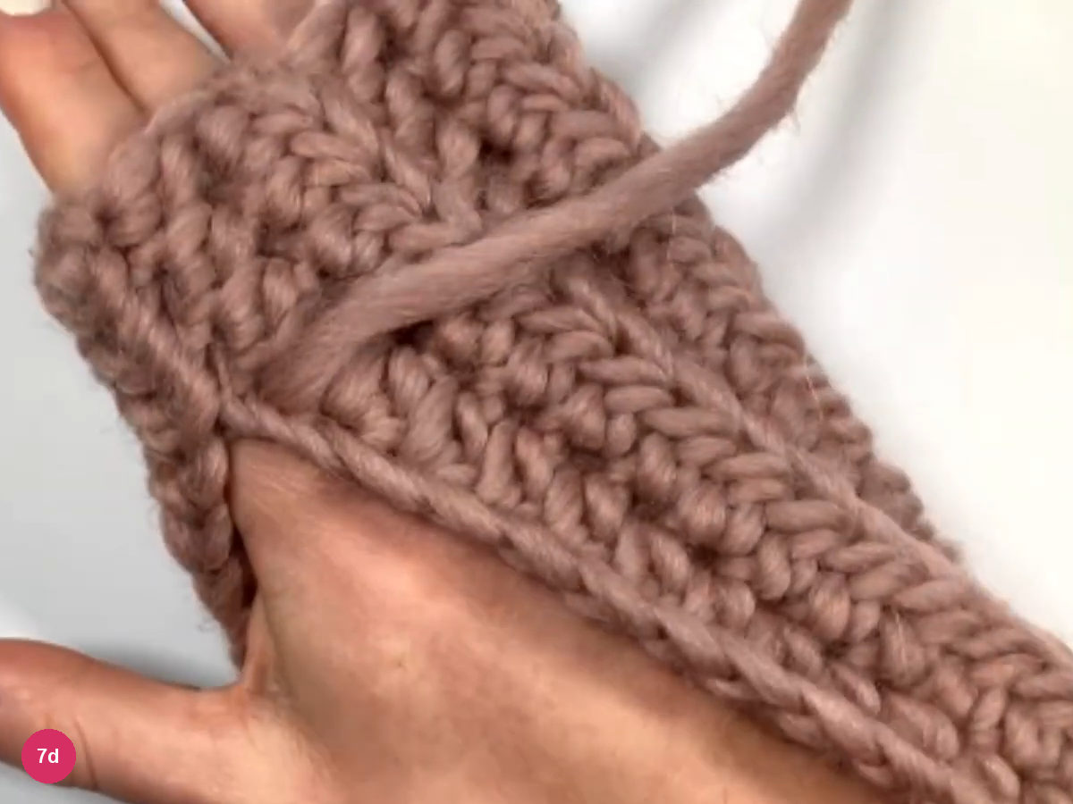 Ribbed fabric curved over a hand, with the yarn tail lying across it, to judge where the thumb will sit