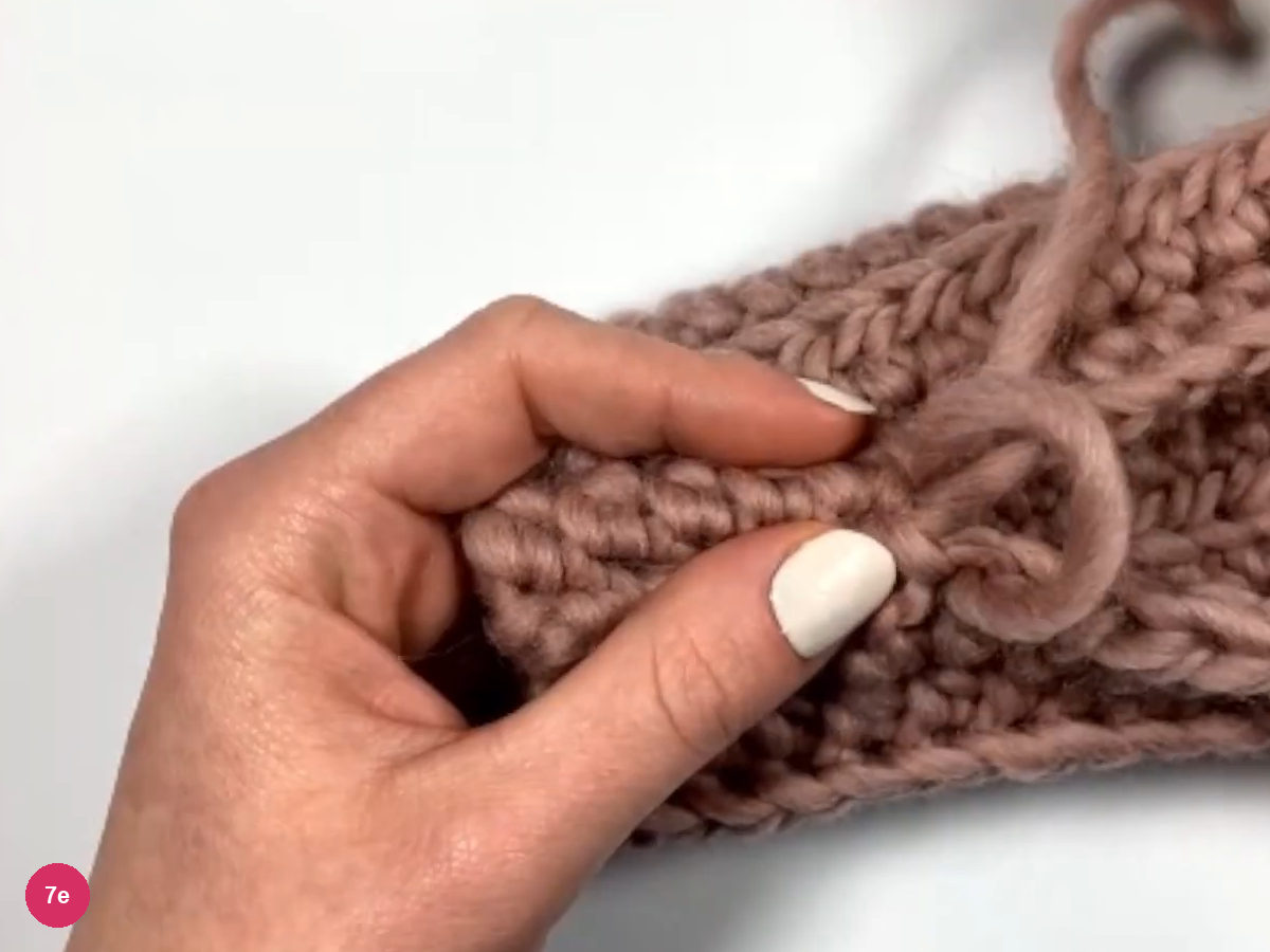 A small yarn loop being tied at the end of the seam, held by the left hand