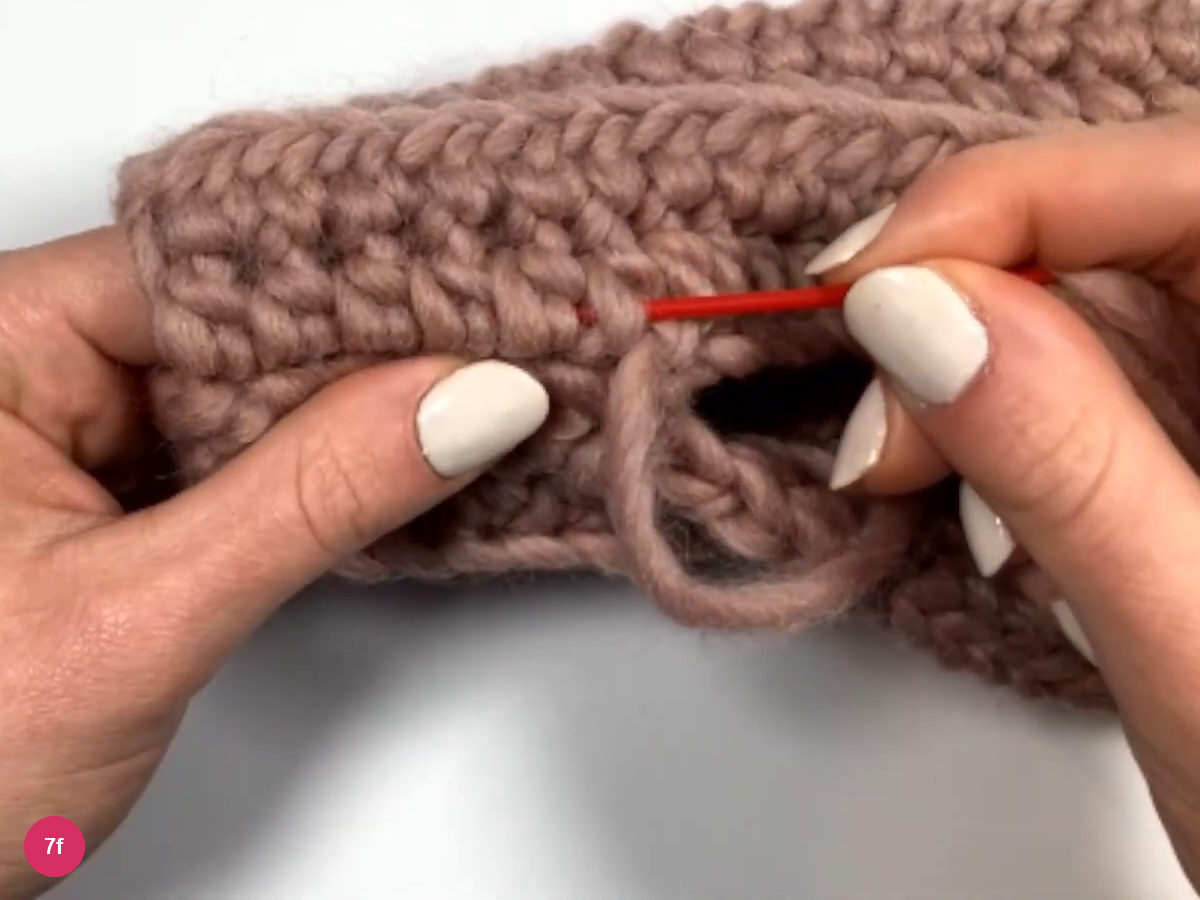 Red needle running under stitches beside the seam with the thumb gap visible below