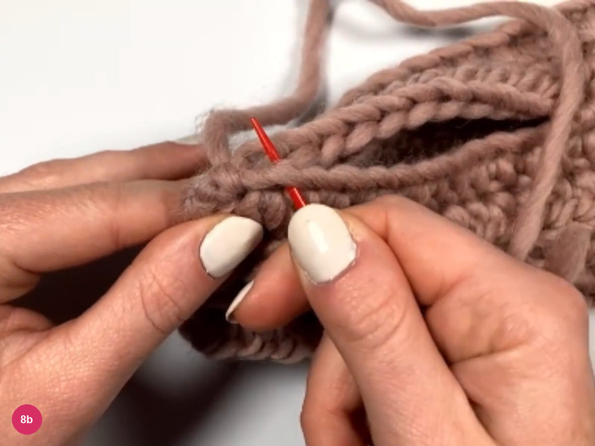 Red needle at the end of the seam beside the open gap, with fingers pinching the edges