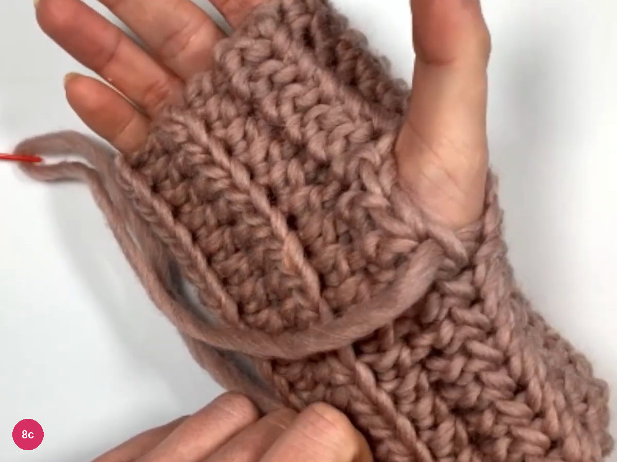 A hand inside the sewn sleeve with a yarn tail and the red needle at the left edge