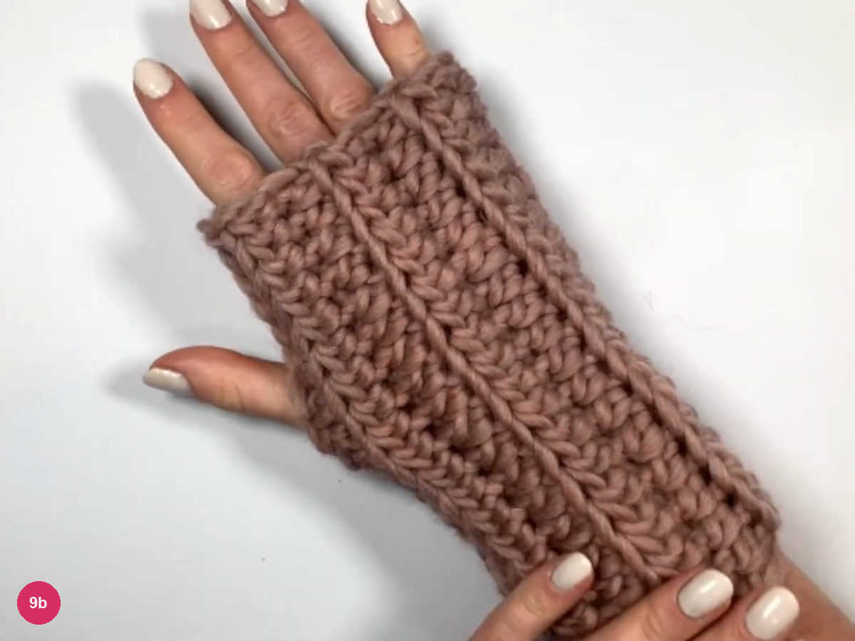 A hand wearing the finished rose ribbed glove with its thumb out through the opening