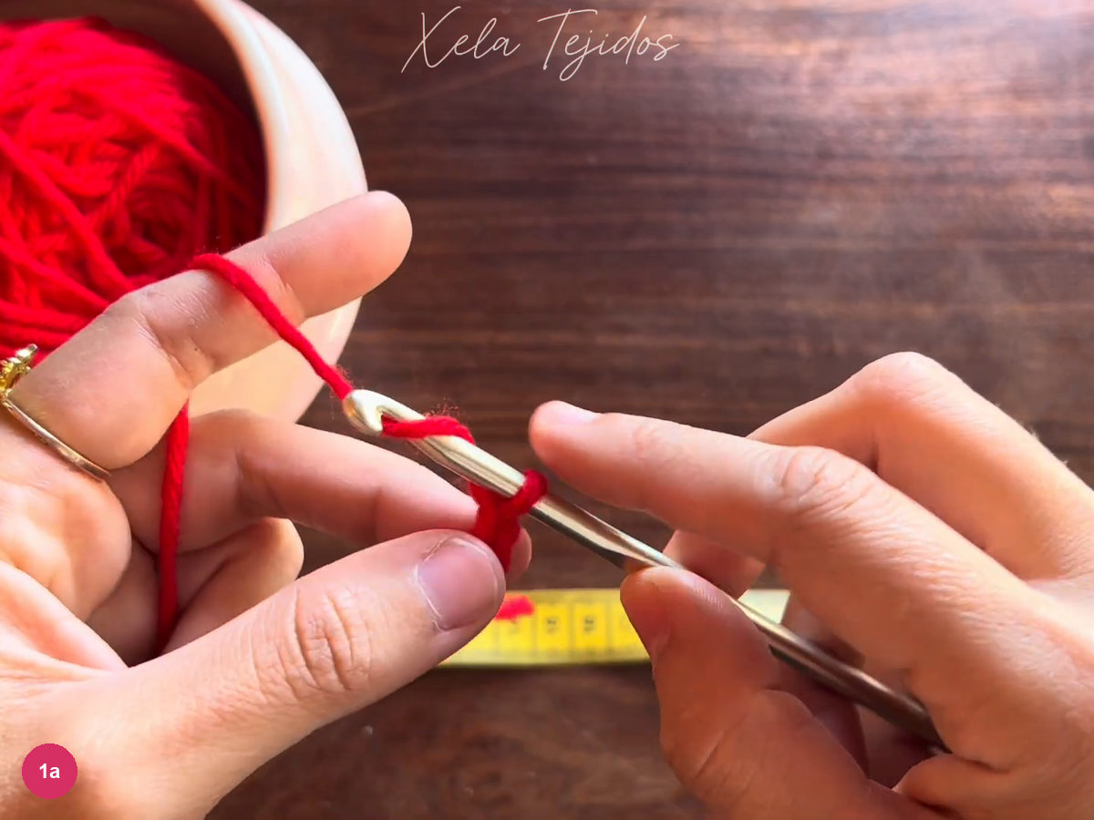 Metal hook drawing red yarn through a starting chain loop