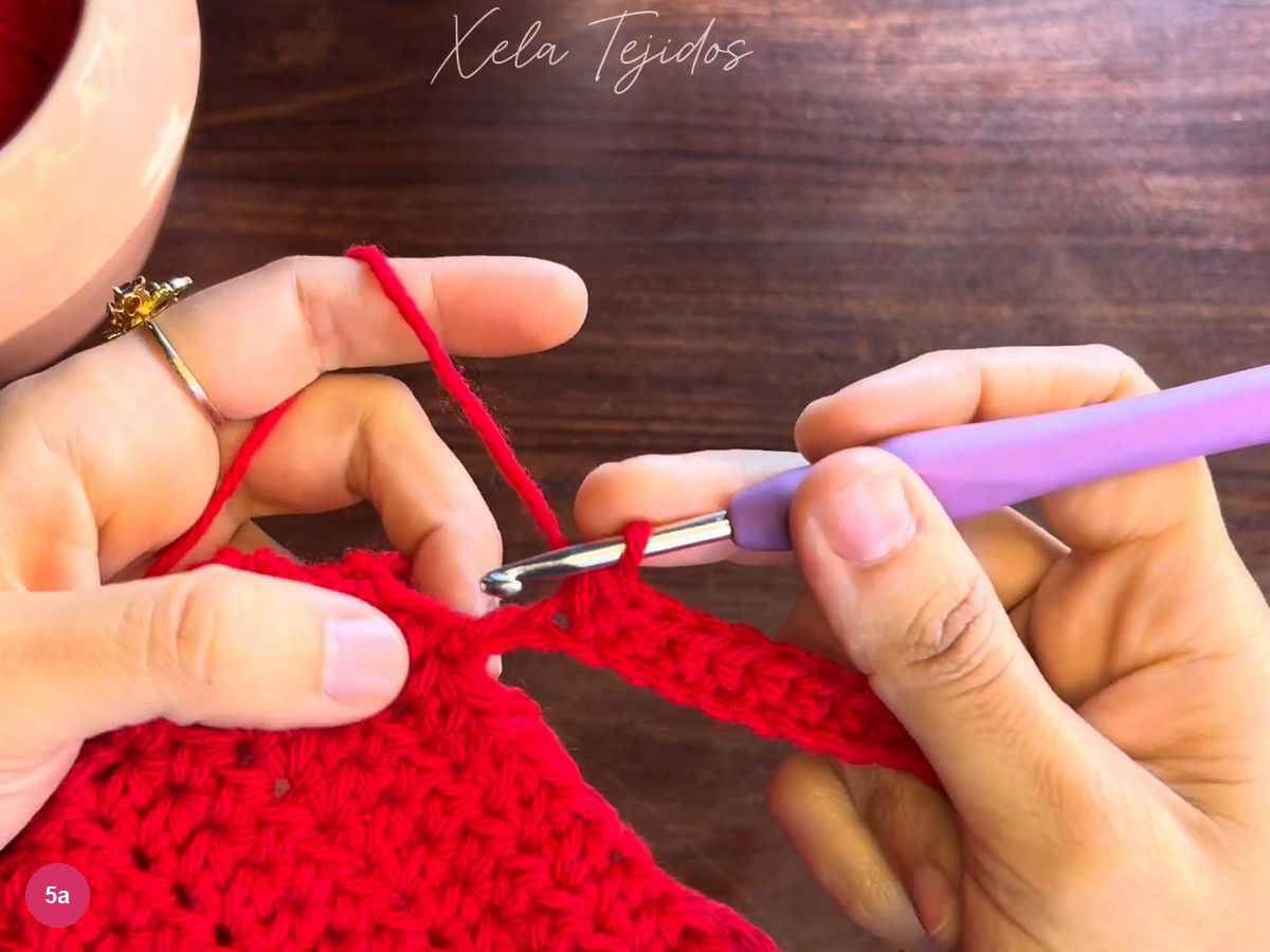 Hook beside the last stitch of the red cuff strip where it meets the body
