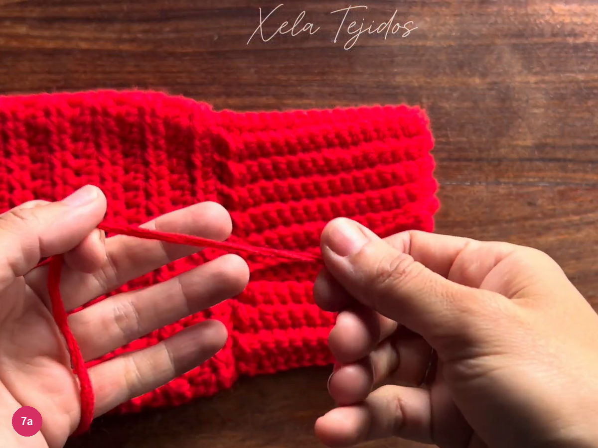 A completed red body and ribbed cuff section on the table with a loose yarn tail