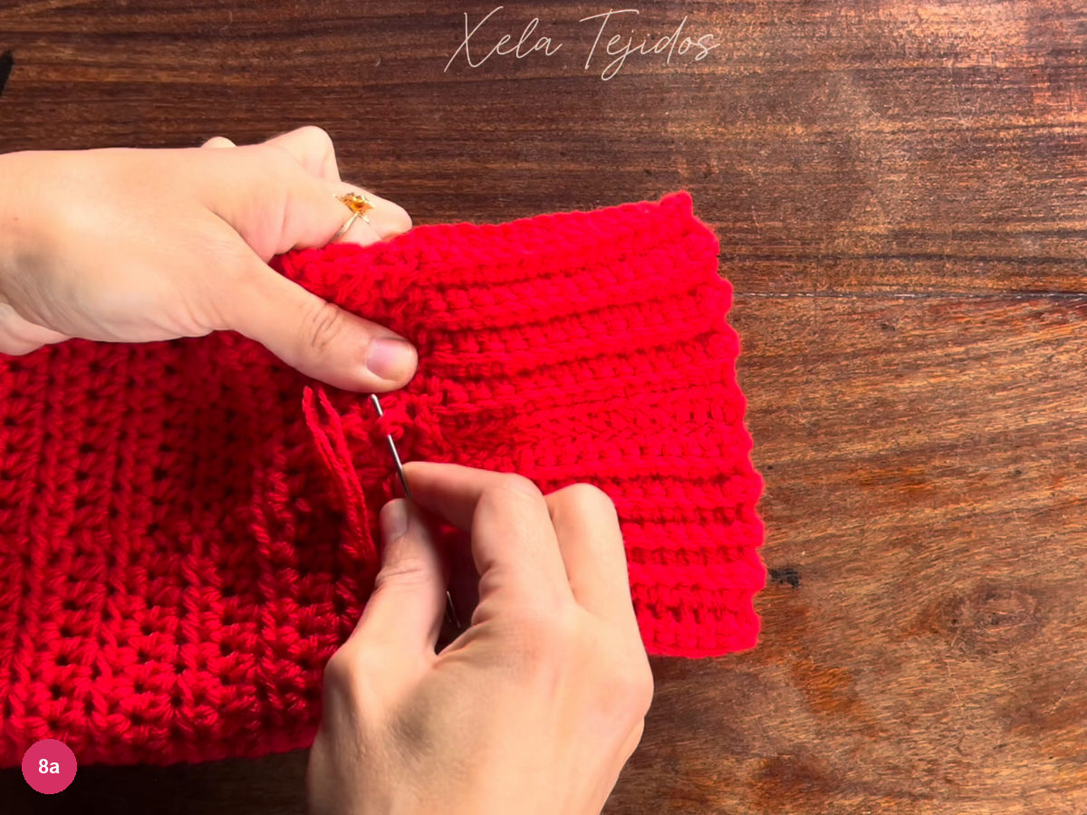 Yarn needle passing a red tail through stitches near the cuff join