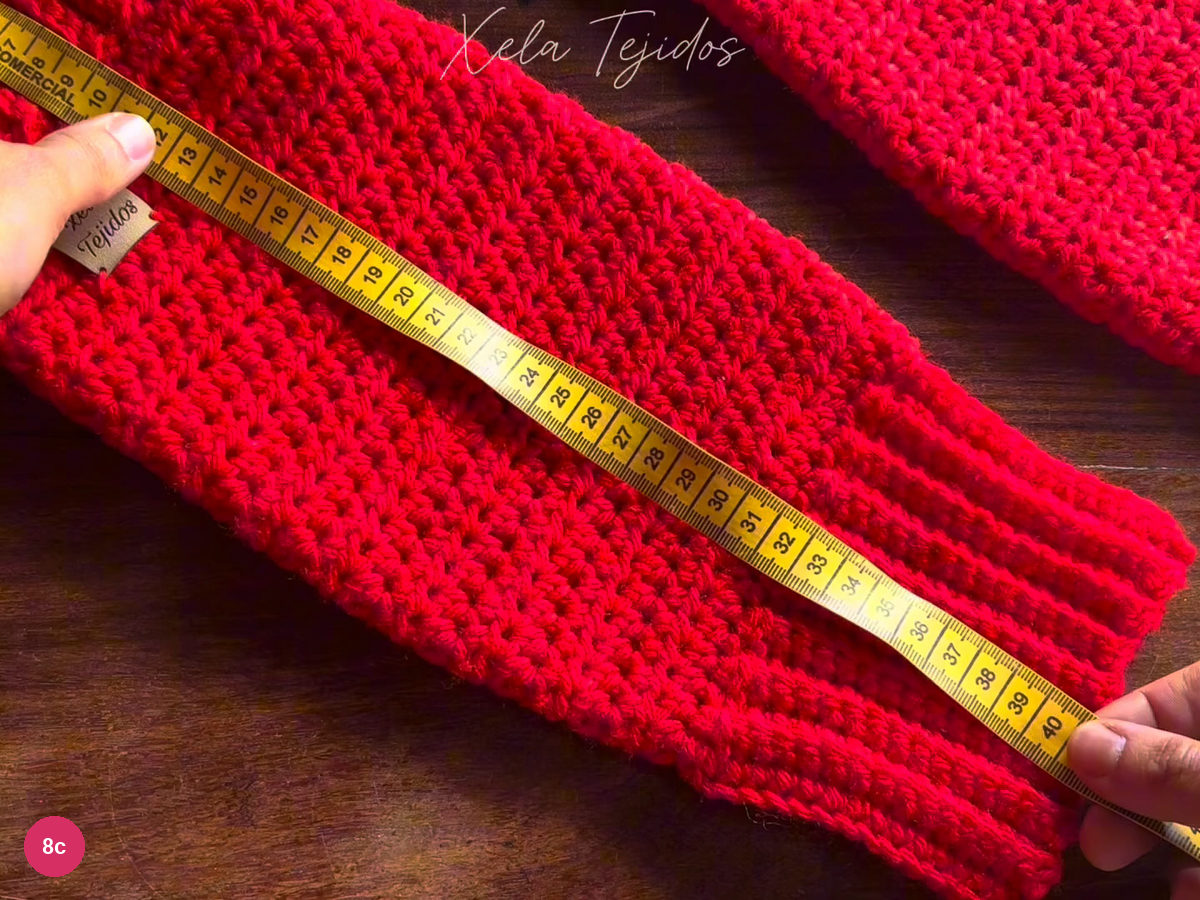 Yellow measuring tape laid along the completed red leg warmer from cuff to cuff