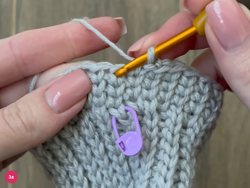 Hook beside a purple stitch marker placed in the first stitch of the round on the cuff top