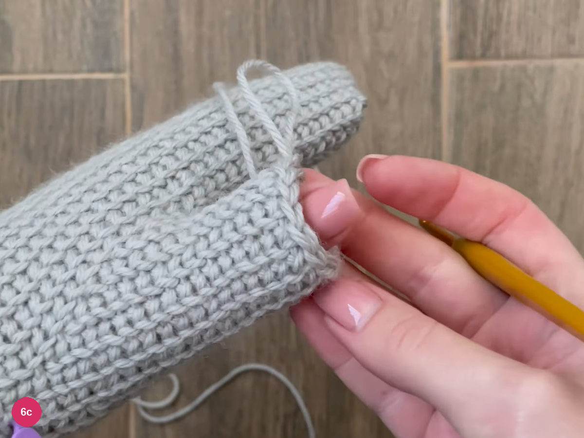 Thumb tube of single crochet with a yarn loop lying along it, held above the mitten