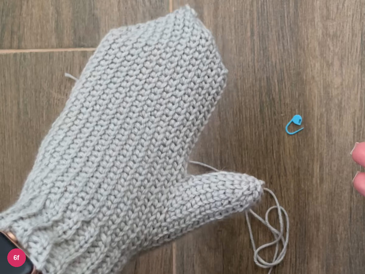 Finished grey crochet mitten laid flat with the thumb at its side edge
