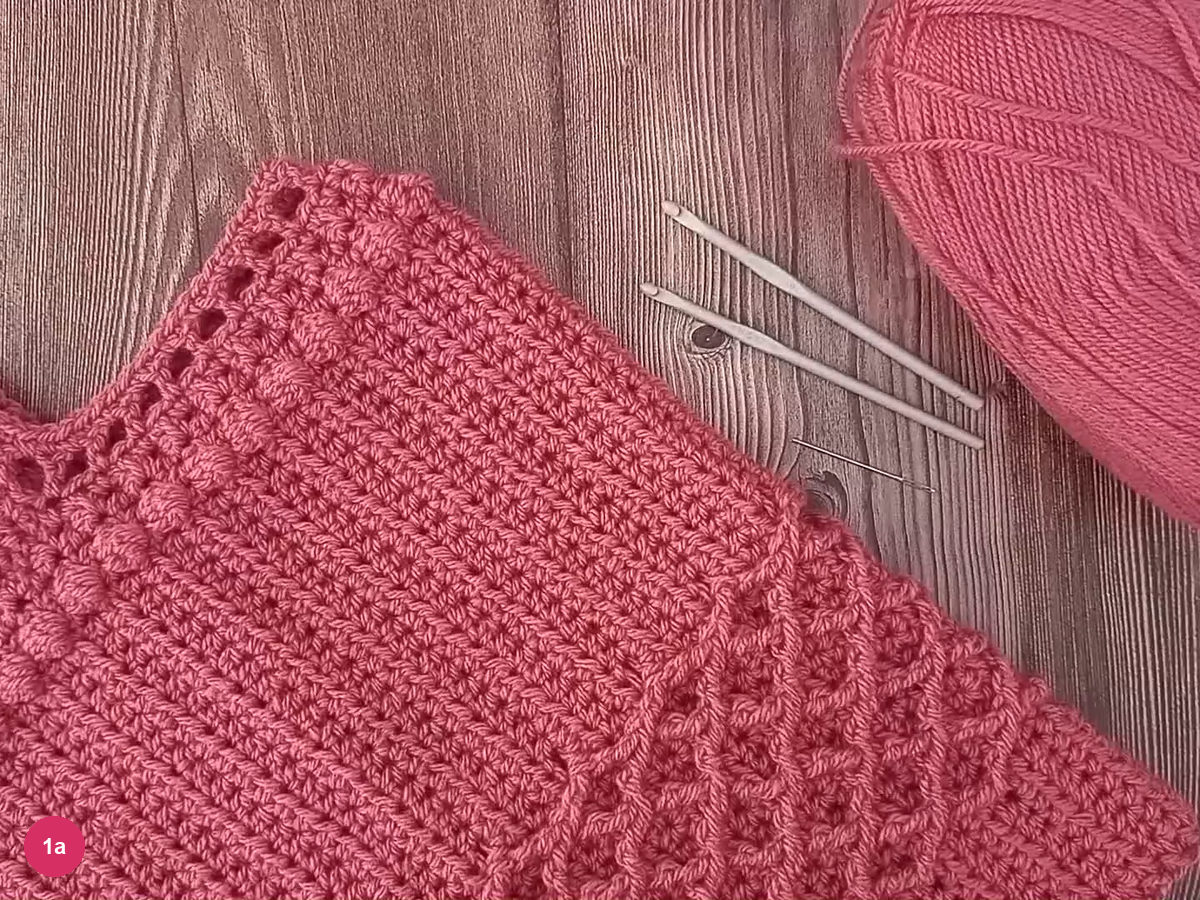 Dusty-rose poncho laid flat with raised diamonds and bobbles beside its V neckline