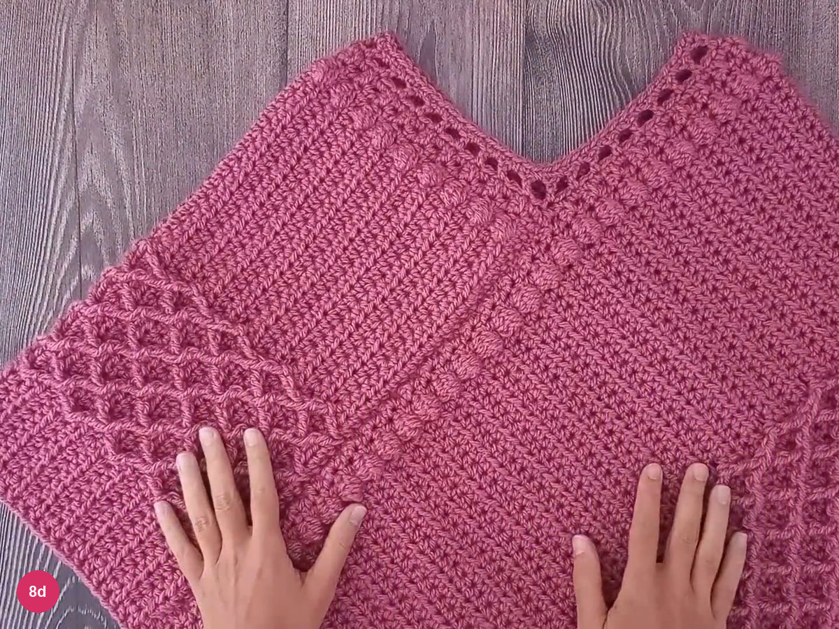 Finished rose poncho with V neckline, raised diamond bands and a plain lower border