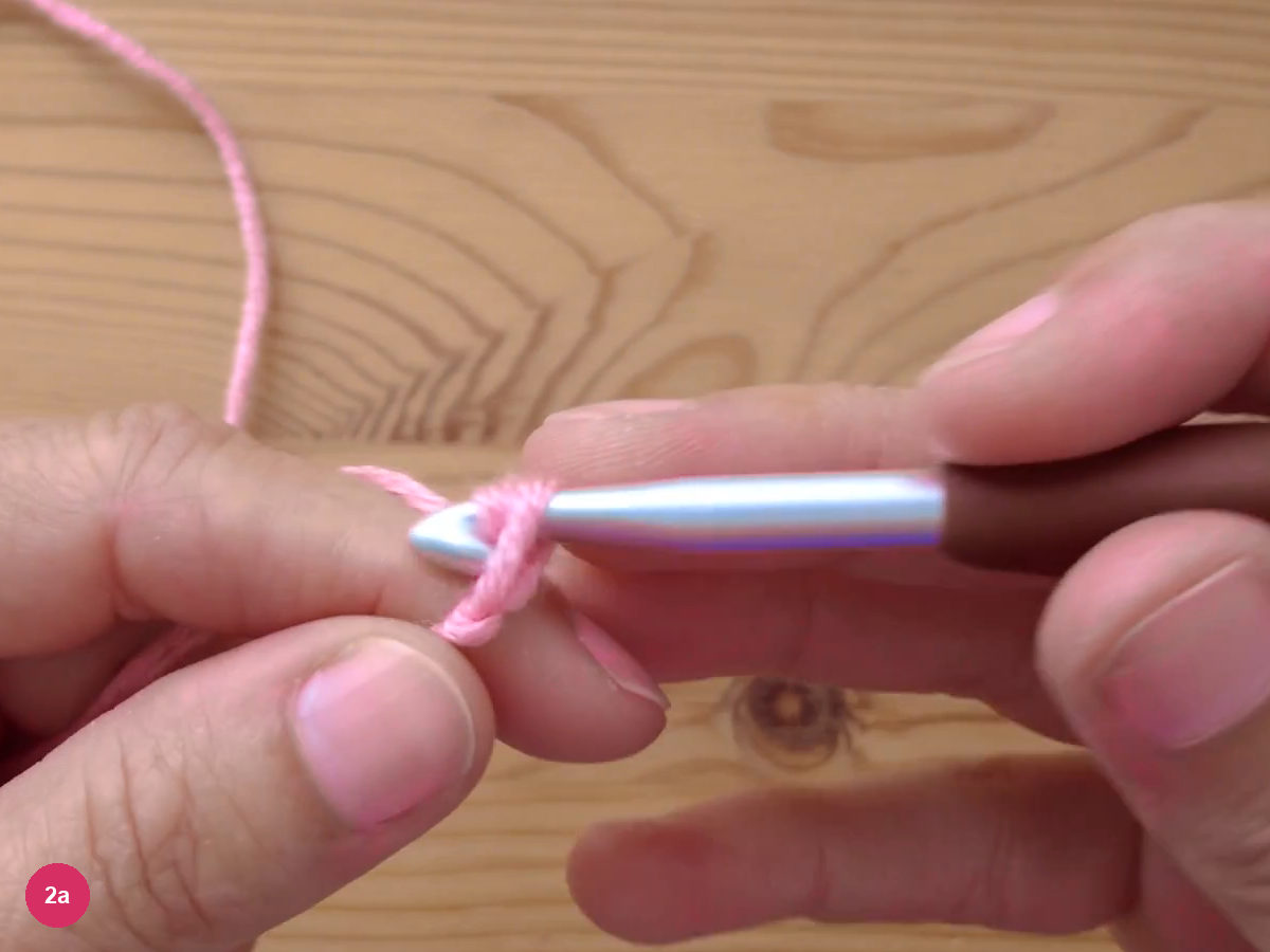 A slip knot sitting on the shank of a crochet hook held between two hands